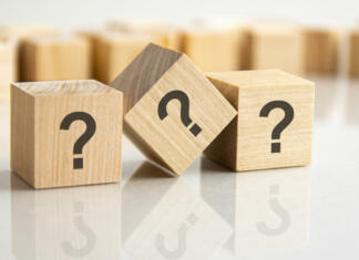 Kako uporabljamo vezaje in pomišljaje three question marks written on wooden cubes lying on the gray table, business and education concept. close-up cubes