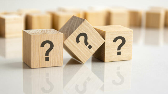 three question marks written on wooden cubes lying on the gray table, business and education concept. close-up cubes