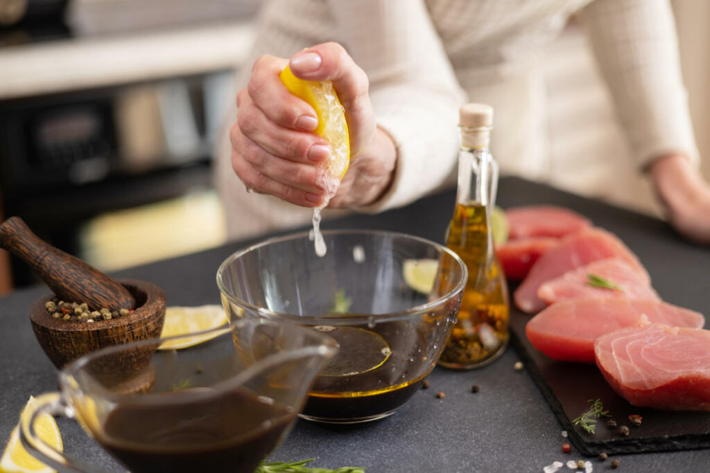 Woman squeezes fresh lemon juice into glass bowl with soy sauce and olive oil making marinade to marinate Pieces of Fresh tuna Fish fillet.