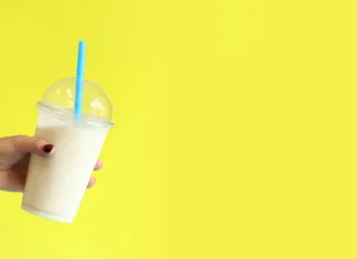 3 esencialne sladice, ki jih mora poskusiti vsak Banana smoothie with plastic disposable cup. Banana milkshake in a girl's hand on a bright yellow background. Copy space