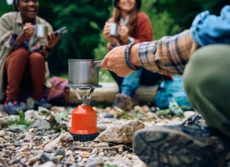 Obroki, ki jih lahko pripraviš na gorilniku + triki za pripravo Close up of hiker preparing a drink on portable gas burner while camping with friends in the forest.