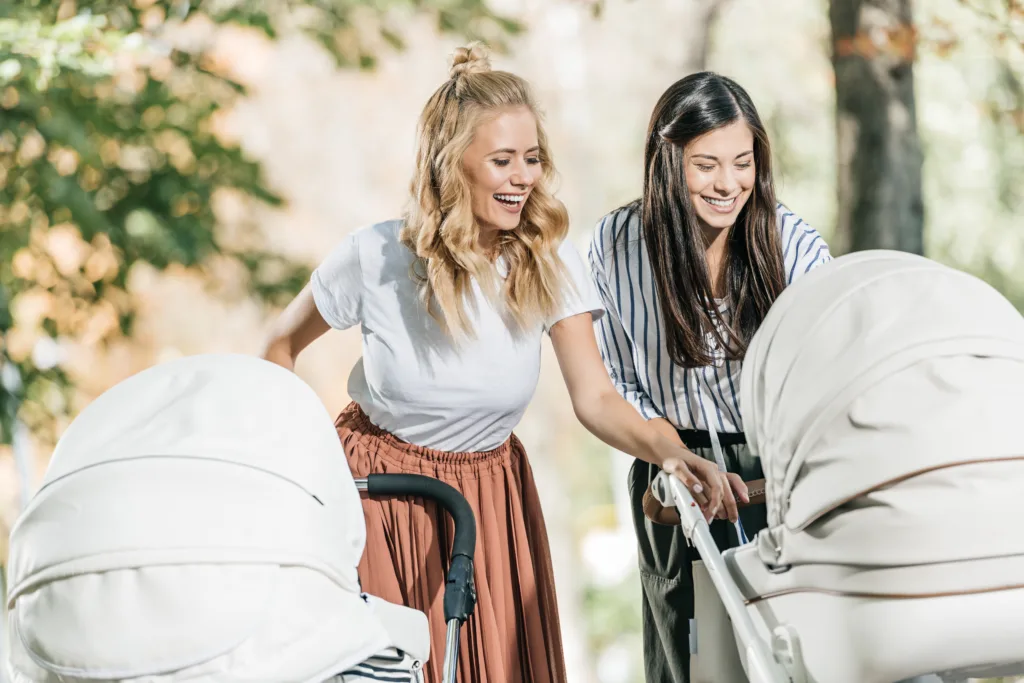 laughing mothers looking in baby stroller in park