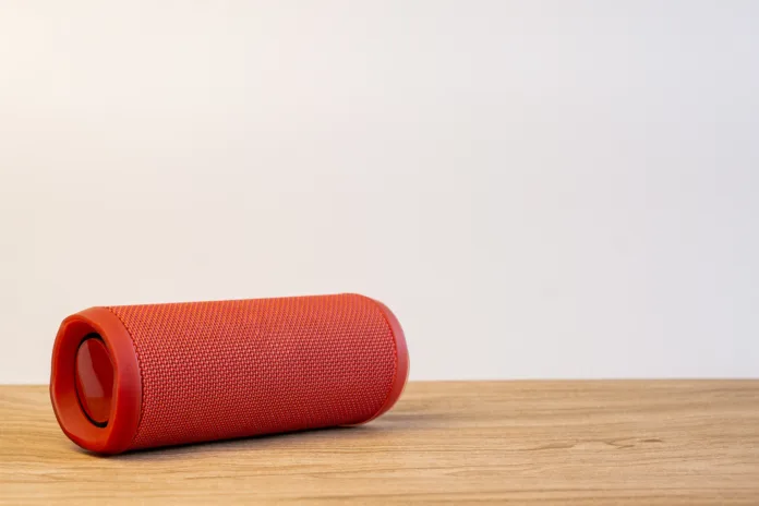 Red bluetooth speaker on wooden table with white background. Space for texture.