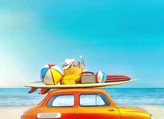 5 poceni destinacij za poletje 2024 Small retro car with baggage, luggage and beach equipment on the roof, fully packed, ready for summer vacation, concept of a road trip with family and friends, dream destination, very vivid colors with dominant blue sky and ocean and bright orange car.