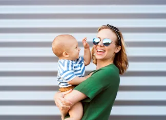 Prednosti mlade nosečke in mamice Young woman with a baby boy standing against the wall. Beautiful mother holding her son in arms.