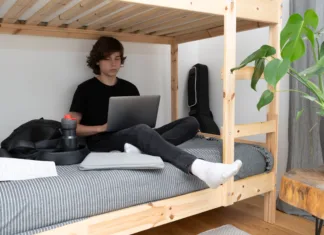 Študenti, ne pozabite na ta pomemben rok! A teenage schoolboy or student is sitting on the lower tier of a bunk bed in his room with a laptop in his hands and doing homework.