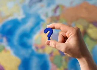 Koliko enklav je na svetu? Adult hand holding question mark plastic toy on the world political map background. Travel planning explore destination concept. Quarantine over, borders open