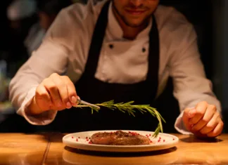 Sestavine, na katere prisegajo kuharski mojstri, mi pa jih spregledamo Hand of young male chef putting aromatic herb on top of roasted meat seasoned with spices while preparing tasty dish for serving