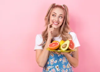 7 pozitivnih učinkov, ki jih čutimo, če vsak dan jemo sadje Photo of minded nice woman dressed print overall hold plate with fruits look empty space finger teeth isolated on pink color background.