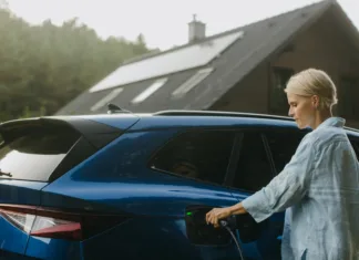 Kako do subvencije za električne avtomobile? Vse o nepovratni finančni spodbudi za električne avtomobile Portrait of woman charging electric car in front of her house with solar panels on roof. Mother plugging charger into the charging port. Solar energy and sustainable lifestyle of young family.