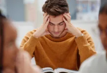 Največja napaka pri učenju, ki jo dela skoraj vsak študent Study, stress and student at university with anxiety for a test. Young man with headache, worried and studying with textbook on desk in library. Focus in education, learning and stressed about exam