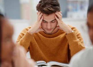 Največja napaka pri učenju, ki jo dela skoraj vsak študent Study, stress and student at university with anxiety for a test. Young man with headache, worried and studying with textbook on desk in library. Focus in education, learning and stressed about exam