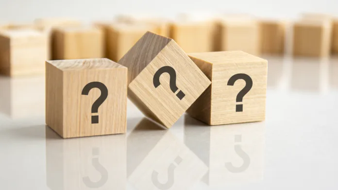 three question marks written on wooden cubes lying on the gray table, business and education concept. close-up cubes