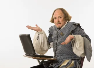 Shakespearove fraze, ki jih uporabljamo še danes William Shakespeare in period clothing sitting in school desk with laptop computer shrugging at viewer.