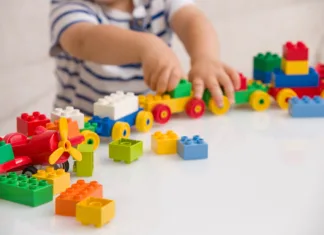 Pozor! To je plastična snov, ki naj bi pri plodu povzročala avtizem Close up of child's hands playing with colorful plastic bricks at the table. Toddler having fun and building out of bright constructor bricks. Early learning. stripe background. Developing toys