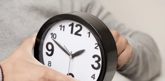 closeup of a young caucasian man adjusting the time of a clock