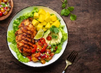 Pripravi se na nov vročinski val: 3 zdravi in lahki poletni obroki Grilled chicken with side dish salad from avocado, mango, tomato salsa, cilantro, lime and lettuce, rustic wooden table background, top view