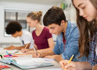 Kaj lahko narediš sam pred novim šolskim letom? Group of college students studying in classroom writing notes during lesson. Focused guy and girls studying in college library sitting at desk. Group of multiethnic university students doing research sitting in a row.