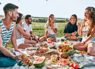 Seznam esencialnih stvari, ki jih moraš imeti na pikniku Group of young attractive friends having a picnic, sitting on a grey blanket on green grass
