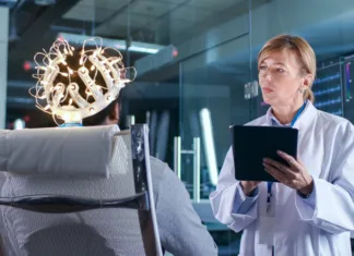 Bi lahko bila ta terapija odgovor za mnoge bolnike s Parkinsonovo boleznijo? Man Wearing Brainwave Scanning Headset Sits in a Chair while Scientist with Tablet Computer Supervises Process. In the Modern Brain Study Laboratory Monitors Show EEG Reading and Brain Model.
