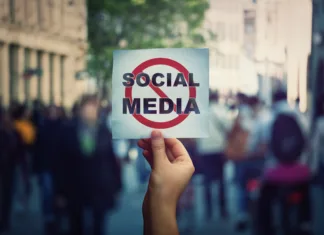Komentar: Svobodo govora lahko reši le ukinitev družbenih omrežij Social media censorship, political war between US president banning social networks. Hand holding a banner with forbidden sign over a crowded street background. Internet communication risk concept.