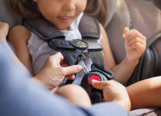 Najnovejši dosežek na področju otroške varnosti v prometu A toddler sitting in the child car seat with the mother helping to buckle and fasten seat beat properly to stay safe while driving.