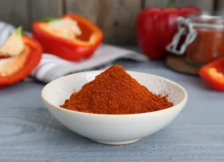 Sladka paprika: Kdaj jo dodati in kako uporabljati? Bowl with aromatic paprika powder and fresh bell peppers on grey wooden table
