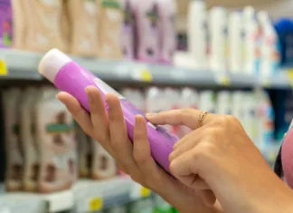 Aplikacija Codecheck: Ali so izdelki varni? Close-up of a young woman's hands reading information on a bottle of shower gel in a store. Buying cosmetics in the store. Shopping trip.