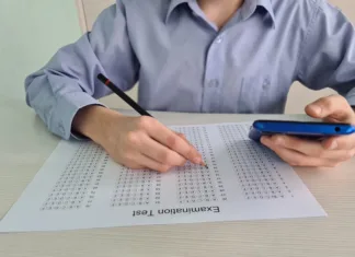 Kako statistična analiza prepozna uporabo ChatGPT? Closeup of teenager sitting at desk holding phone in her hand and taking exam test. Focused guy preparing for test or college exam