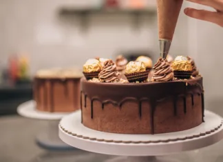 Skrivnosti vrhunskih slaščičarjev: kako pripraviti odlično torto? Confectioner decorating chocolate cake, close-up.