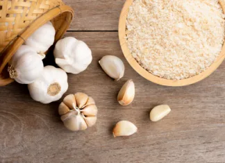 Vodič po začimbah: česen v prahu Garlic powder in wooden bowl and bulb of garlic isolated on wooden table background. Top view. Flat lay.