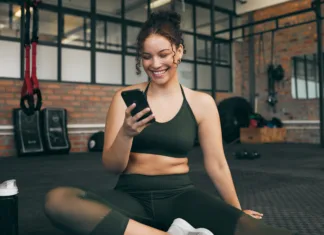 Skrita tveganja ženskih zdravstvenih aplikacij Happy woman, fitness and phone at gym for a workout, training and body wellness with a mobile app. Sports female with smartphone for progress, performance and communication for a healthy lifestyle