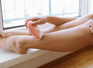 Nega za ženske: 3 pripomočki, ki jih mora imeti vsaka ženska woman takes care herself, depilates legs with an epilator, sits on parquet floor, put legs on threshold near window, sun's rays on skin. Epilation cosmetic procedure for removing hair. SPA concept.