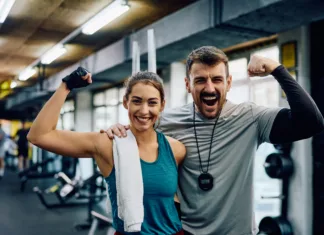 Kako telesna aktivnost vpliva na duševno zdravje mladih Happy athletic woman and her fitness instructor flexing muscles in a gym while looking at camera.