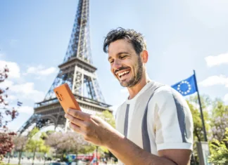 Skrita past gostovanja v tujini: če ste premalo doma, vas čakajo doplačila Happy tourist booking hotel with smart mobile phone device in Paris, France - Handsome young man using date app with smartphone - Travel, technology and youth concept
