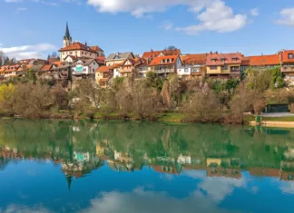 Kam na Teden restavracij na Dolenjskem? Novo Mesto, Slovenia - March 6, 2020: Houses Reflection at Calm Surface of River Krka Clear Winter Day in Town.