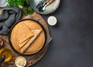 Vse o palačinkah: zgodovina, izvor in priljubljenost v Sloveniji in po svetu Stack pancakes on a dark background with honey, sour cream and nuts. Russian blini. Mardi Gras. Top view, copy space.