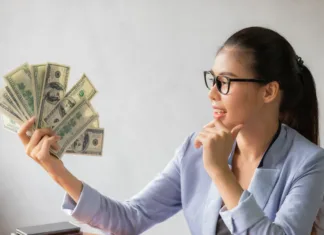 Si finančno neodvisen? Kaj finančna neodvisnost sploh pomeni? Successful Asian business young woman holding money US dollar bills in hand on office desk, business finance concept
