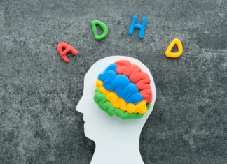ADHD je lahko povezan z otroškimi izpadi A brain model crafted from colorful materials rests on a white head silhouette, with the letters ADHD on a concrete background.