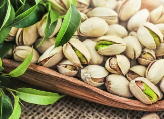 Si s tem prigrizkom res lahko izboljšaš vid? Bowl with pistachios nut on a wooden table with green leaves. Pistachio nuts detail..