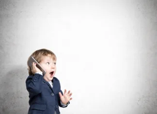 Za najmlajše: Kako deluje telefonski klic? Cute little child is talking on his smartphone while standing in his business suit near a concrete wall. Mock up