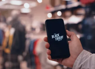 Za Črni petek raje kupi tole in ne bo ti žal Online shopping on Black Friday. A man holds a smartphone in his hands against the background of a fashionable clothing boutique