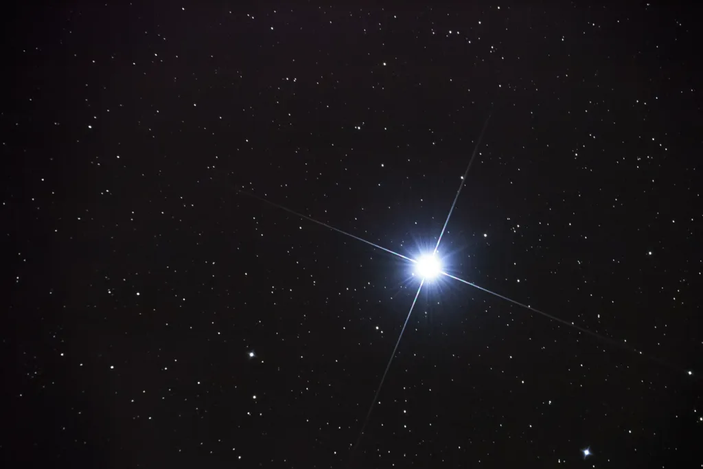 This is a real photo of a star taken through a telescope. It was taken for the purpose of focusing. The cross (plus) over the star is due to the central obstruction of the telescope (a frame holding the secondary mirror in place). The star is Vega, one of the brightest stars in the northern night sky. Vega used to be a North Pole star some 20 000 years ago.