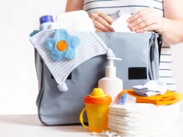 Unrecognizible pregnant caucasian woman in striped t-shirt packing big blue diaper bag to maternity hospital. Diapers, nappy, hat, bottle and other necessary things for newborn baby.