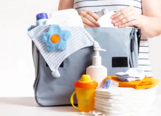 5 esencialnih pripomočkov, ki jih morajo imeti mladi starši Unrecognizible pregnant caucasian woman in striped t-shirt packing big blue diaper bag to maternity hospital. Diapers, nappy, hat, bottle and other necessary things for newborn baby.