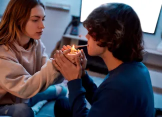 Raziskava razkriva: Konoplja uničuje ključne povezave v možganih mladih odraslih Young girl lighting cannabis cigarette for her boyfriend while sitting on the couch at home. Young couple smoking marijuana joint and relaxing. Marijuana, drugs, cannabis and weed legalization