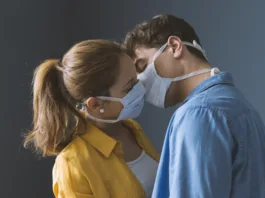 Young millennials couple wearing protective face masks and kissing each other, virus spread prevention and people concept
