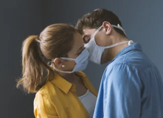 Presenetljiv trend: Se zaradi koronavirusa manj poljubjamo? Young millennials couple wearing protective face masks and kissing each other, virus spread prevention and people concept