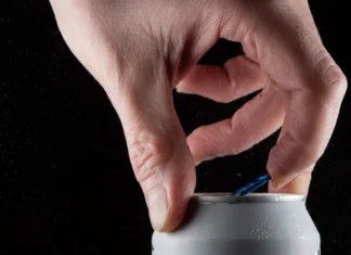 Koliko časa zdržijo alkoholne pijače, ko jih odpremo? A man's hand opening a soda can on a black background and showing the splash when opening the can.