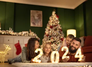 Dekoracijski trendi, ki bodo zaznamovali letošnji božič Parents and children having fun celebrating New Year together at home, lying by the Christmas tree holding illuminative numbers 2024